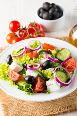 Kiraz domates, ruccola, roka, beyaz peynir, zeytin, salatalık, soğan ve baharat taze Yunan salatası yaptı. Sezar salatası ahşap arka plan üzerinde beyaz bir kase. Sağlıklı organik beslenme gıda kavramı.