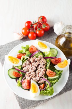 Domates, roka, ton balığı, yumurta, roka, kraker ve baharattan yapılmış taze balık salatası. Tahta arka planda beyaz bir kasede Sezar salatası.