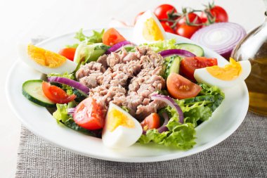 Domates, roka, ton balığı, yumurta, roka, kraker ve baharattan yapılmış taze balık salatası. Tahta arka planda beyaz bir kasede Sezar salatası.