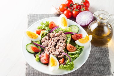 Domates, roka, ton balığı, yumurta, roka, kraker ve baharattan yapılmış taze balık salatası. Tahta arka planda beyaz bir kasede Sezar salatası.