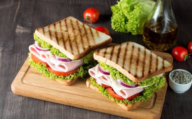 Club sandviç yakın çekim fotoğraf. Eti, jambon, salam, salata, sebze, marul, domates, soğan ve hardal ahşap arka plan üzerinde taze dilimlenmiş siyah ekmek üzerinde sandviç. Zeytin arka plan.