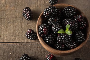 Ahşap arka plan üzerinde ahşap bir kase taze organik olgun böğürtlen. Sağlıklı rustik gıda konsepti.