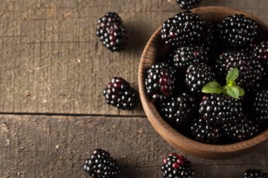 Ahşap arka plan üzerinde ahşap bir kase taze organik olgun böğürtlen. Sağlıklı rustik gıda konsepti.