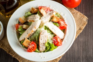 Taze salata domates, ruccola, tavuk göğsü, yumurta, roka, kraker ve baharat yapılmış. Ahşap arka plan üzerinde beyaz, şeffaf bir kasede Sezar salatası