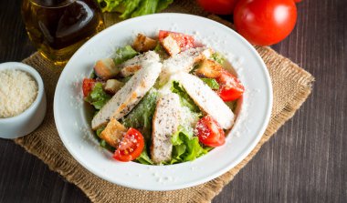 Taze salata domates, ruccola, tavuk göğsü, yumurta, roka, kraker ve baharat yapılmış. Ahşap arka plan üzerinde beyaz, şeffaf bir kasede Sezar salatası