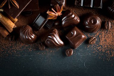 Koyu, beyaz ve sütlü çikolata yığını, cips çeşitleri. Kaba ahşap arka planda çikolata ve kahve çekirdekleri. Baharatlar, tarçın. Seçici makro odaklanma. Çikolata arkaplanı. Tatlılar