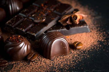 Koyu, beyaz ve sütlü çikolata yığını, cips çeşitleri. Kaba ahşap arka planda çikolata ve kahve çekirdekleri. Baharatlar, tarçın. Seçici makro odaklanma. Çikolata arkaplanı. Tatlılar