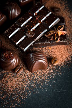 Koyu, beyaz ve sütlü çikolata yığını, cips çeşitleri. Kaba ahşap arka planda çikolata ve kahve çekirdekleri. Baharatlar, tarçın. Seçici makro odaklanma. Çikolata arkaplanı. Tatlılar