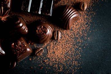 Koyu, beyaz ve sütlü çikolata yığını, cips çeşitleri. Kaba ahşap arka planda çikolata ve kahve çekirdekleri. Baharatlar, tarçın. Seçici makro odaklanma. Çikolata arkaplanı. Tatlılar