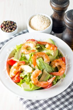 Domates, ruccola, avokado, karides, tavuk göğsü, arugula, kraker ve baharatyapılmış taze karides salatası. Ahşap arka plan üzerinde beyaz, şeffaf bir kapta Sezar salatası