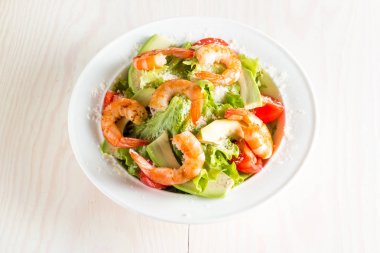 Domates, ruccola, avokado, karides, tavuk göğsü, arugula, kraker ve baharatyapılmış taze karides salatası. Ahşap arka plan üzerinde beyaz, şeffaf bir kapta Sezar salatası