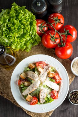 Taze salata domates, ruccola, tavuk göğsü, yumurta, roka, kraker ve baharat yapılmış. Ahşap arka plan üzerinde beyaz, şeffaf bir kasede Sezar salatası