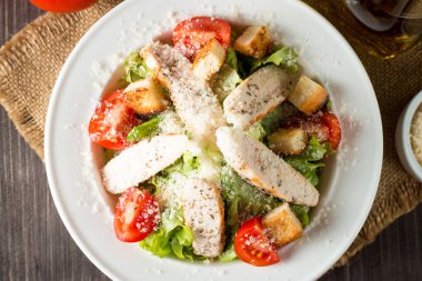 Taze salata domates, ruccola, tavuk göğsü, yumurta, roka, kraker ve baharat yapılmış. Ahşap arka plan üzerinde beyaz, şeffaf bir kasede Sezar salatası