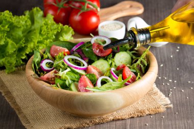 Çeri domates, roka, roka, feta, zeytin, salatalık, soğan ve baharattan yapılmış taze ve sağlıklı sebze salatası. Yunan, Sezar salatası beyaz bir kâse içinde ahşap arka planda. Sağlıklı organik diyet gıda konsepti.