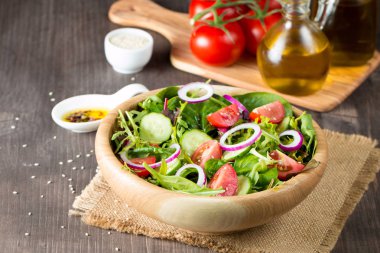 Çeri domates, roka, roka, feta, zeytin, salatalık, soğan ve baharattan yapılmış taze ve sağlıklı sebze salatası. Yunan, Sezar salatası beyaz bir kâse içinde ahşap arka planda. Sağlıklı organik diyet gıda konsepti.