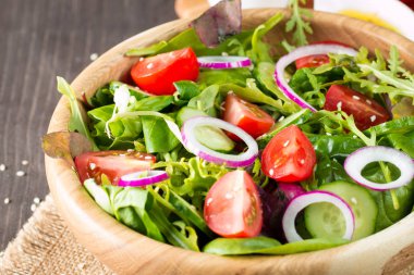 Çeri domates, roka, roka, feta, zeytin, salatalık, soğan ve baharattan yapılmış taze ve sağlıklı sebze salatası. Yunan, Sezar salatası beyaz bir kâse içinde ahşap arka planda. Sağlıklı organik diyet gıda konsepti.