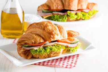 Taze kruvasan veya sandviç salata, jambon, jamon, jambon, salam, peynir, tavuk, domates ahşap arka plan ile. Sabah kahvaltı kavramı. Sağlıklı ve fast food.