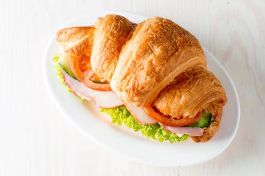 Taze kruvasan veya sandviç salata, jambon, jamon, jambon, salam, peynir, tavuk, domates ahşap arka plan ile. Sabah kahvaltı kavramı. Sağlıklı ve fast food.