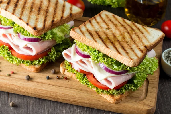 Club sandviç yakın çekim fotoğraf. Eti, jambon, salam, salata, sebze, marul, domates, soğan ve hardal ahşap arka plan üzerinde taze dilimlenmiş siyah ekmek üzerinde sandviç. Zeytin arka plan.