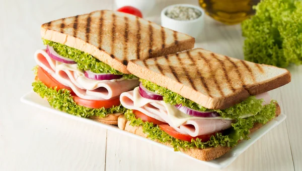 Club sandviç yakın çekim fotoğraf. Eti, jambon, salam, salata, sebze, marul, domates, soğan ve hardal ahşap arka plan üzerinde taze dilimlenmiş siyah ekmek üzerinde sandviç. Zeytin arka plan.