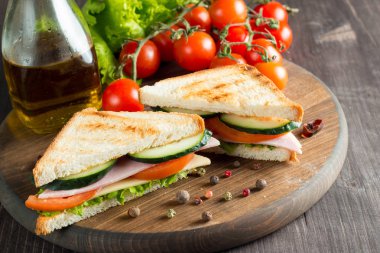 Club sandviç yakın çekim fotoğraf. Eti, jambon, salam, salata, sebze, marul, domates, soğan ve hardal ahşap arka plan üzerinde taze dilimlenmiş siyah ekmek üzerinde sandviç. Zeytin arka plan.