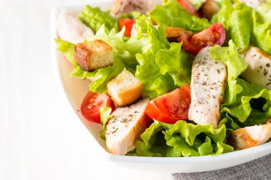 Taze salata domates, ruccola, tavuk göğsü, yumurta, roka, kraker ve baharat yapılmış. Ahşap arka plan üzerinde beyaz, şeffaf bir kasede Sezar salatası