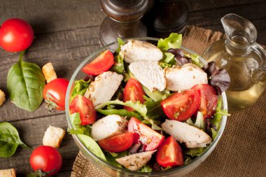 Taze salata domates, ruccola, tavuk göğsü, yumurta, roka, kraker ve baharat yapılmış. Ahşap arka plan üzerinde beyaz, şeffaf bir kasede Sezar salatası