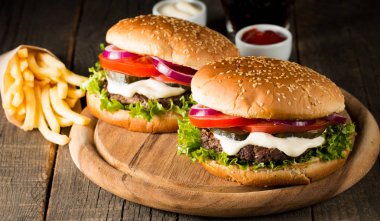 Ev yapımı Hamburger bira ile yakın çekim fotoğraf sığır eti, soğan, domates, marul, peynir ve baharat yaptı. Taze hamburger tatlı patates kızartması ve cips ile ahşap rustik tabloda.