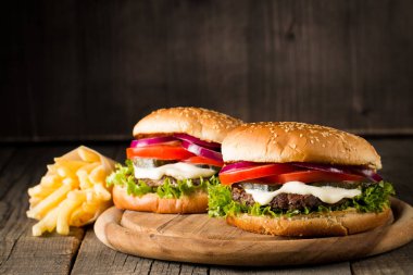 Ev yapımı Hamburger bira ile yakın çekim fotoğraf sığır eti, soğan, domates, marul, peynir ve baharat yaptı. Taze hamburger tatlı patates kızartması ve cips ile ahşap rustik tabloda.