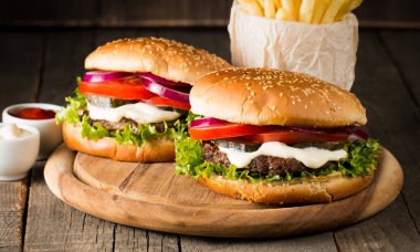 Ev yapımı Hamburger bira ile yakın çekim fotoğraf sığır eti, soğan, domates, marul, peynir ve baharat yaptı. Taze hamburger tatlı patates kızartması ve cips ile ahşap rustik tabloda.