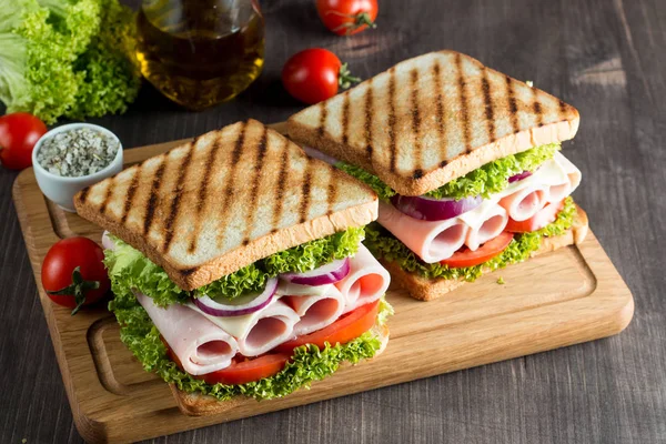 Close-up photo of a club sandwich. Sandwich with meat, prosciutto, salami, salad, vegetables, lettuce, tomato, onion and mustard on a fresh sliced rye bread on wooden background. Olives background.