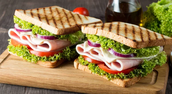 Club sandviç yakın çekim fotoğraf. Eti, jambon, salam, salata, sebze, marul, domates, soğan ve hardal ahşap arka plan üzerinde taze dilimlenmiş siyah ekmek üzerinde sandviç. Zeytin arka plan.