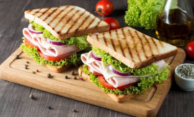 Club sandviç yakın çekim fotoğraf. Eti, jambon, salam, salata, sebze, marul, domates, soğan ve hardal ahşap arka plan üzerinde taze dilimlenmiş siyah ekmek üzerinde sandviç. Zeytin arka plan.