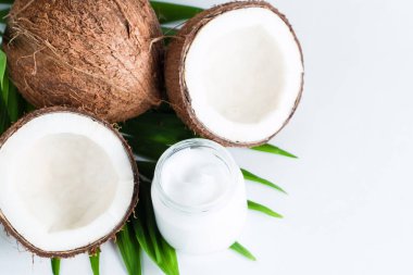 Olgun, yarım kesilmiş hindistan cevizi ve yeşil yapraklı krema beyaz, izole bir zemin. Sağlık ve tıbbi konsept. Cilt bakımı. 