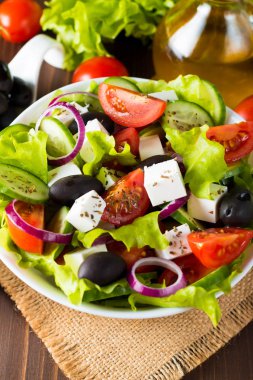 Kiraz domates, ruccola, roka, beyaz peynir, zeytin, salatalık, soğan ve baharat taze Yunan salatası yaptı. Sezar salatası ahşap arka plan üzerinde beyaz bir kase. Sağlıklı organik beslenme gıda kavramı.