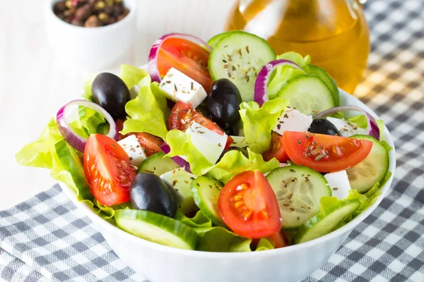 Fresh Greek salad made of cherry tomato, ruccola, arugula, feta, olives, cucumbers, onion and spices. Caesar salad in a white bowl on wooden background. Healthy organic diet food concept.