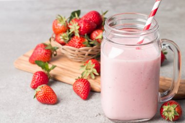 Gri arka planda bir bardak taze çilekli smoothie. Yaz içeceği, milkshake ve ferahlatıcı organik konsept..