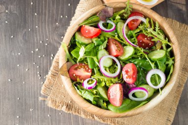 Çeri domates, roka, roka, feta, zeytin, salatalık, soğan ve baharattan yapılmış taze ve sağlıklı sebze salatası. Yunan, Sezar salatası beyaz bir kâse içinde ahşap arka planda. Sağlıklı organik diyet gıda konsepti.