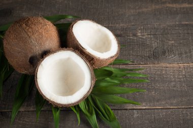 Ahşap arka planda yeşil yapraklı, yarım kesilmiş hindistan cevizi.. 