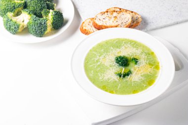 Sıcak ve rahatlatıcı kremalı brokoli çorbası bir kasede servis edilir, parmesan peyniri ve kızarmış ekmekle süslenir..