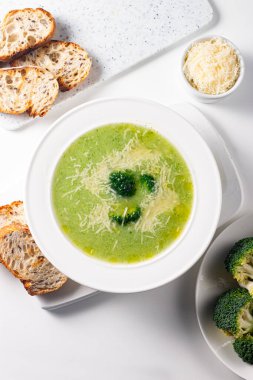 Sıcak ve rahatlatıcı kremalı brokoli çorbası bir kasede servis edilir, parmesan peyniri ve kızarmış ekmekle süslenir..