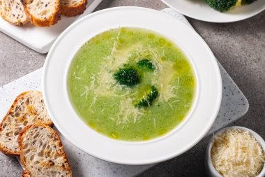 Sıcak ve rahatlatıcı kremalı brokoli çorbası bir kasede servis edilir, parmesan peyniri ve kızarmış ekmekle süslenir..