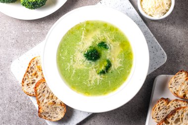 Sıcak ve rahatlatıcı kremalı brokoli çorbası bir kasede servis edilir, parmesan peyniri ve kızarmış ekmekle süslenir..