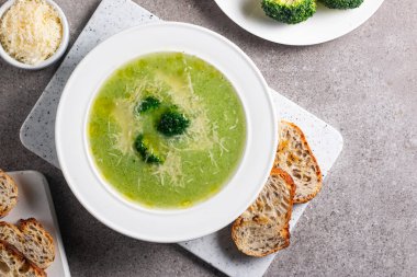 Sıcak ve rahatlatıcı kremalı brokoli çorbası bir kasede servis edilir, parmesan peyniri ve kızarmış ekmekle süslenir..