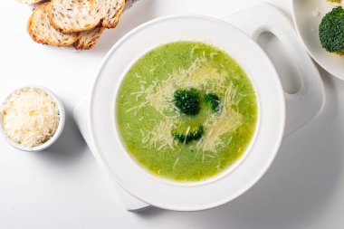 Sıcak ve rahatlatıcı kremalı brokoli çorbası bir kasede servis edilir, parmesan peyniri ve kızarmış ekmekle süslenir..