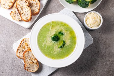 Sıcak ve rahatlatıcı kremalı brokoli çorbası bir kasede servis edilir, parmesan peyniri ve kızarmış ekmekle süslenir..