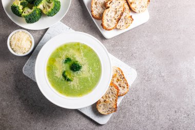 Sıcak ve rahatlatıcı kremalı brokoli çorbası bir kasede servis edilir, parmesan peyniri ve kızarmış ekmekle süslenir..