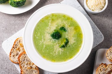 Sıcak ve rahatlatıcı kremalı brokoli çorbası bir kasede servis edilir, parmesan peyniri ve kızarmış ekmekle süslenir..