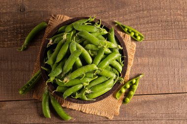 Tahta masadaki bir kasede taze bezelye ve kabuklar. Sebzeli sağlıklı yiyecek..  