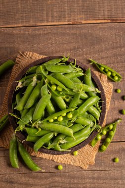 Tahta masadaki bir kasede taze bezelye ve kabuklar. Sebzeli sağlıklı yiyecek..  